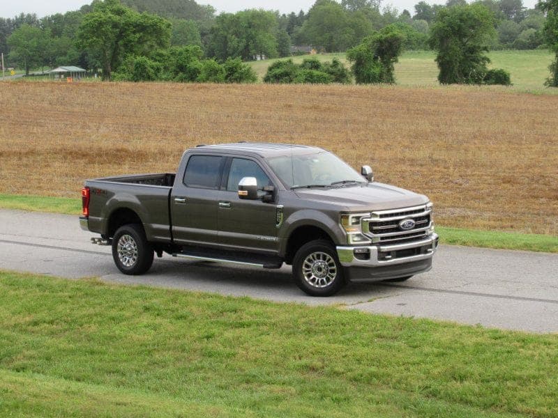A grey Ford F-250 crew cab pickup truck parked on a road beside a field.