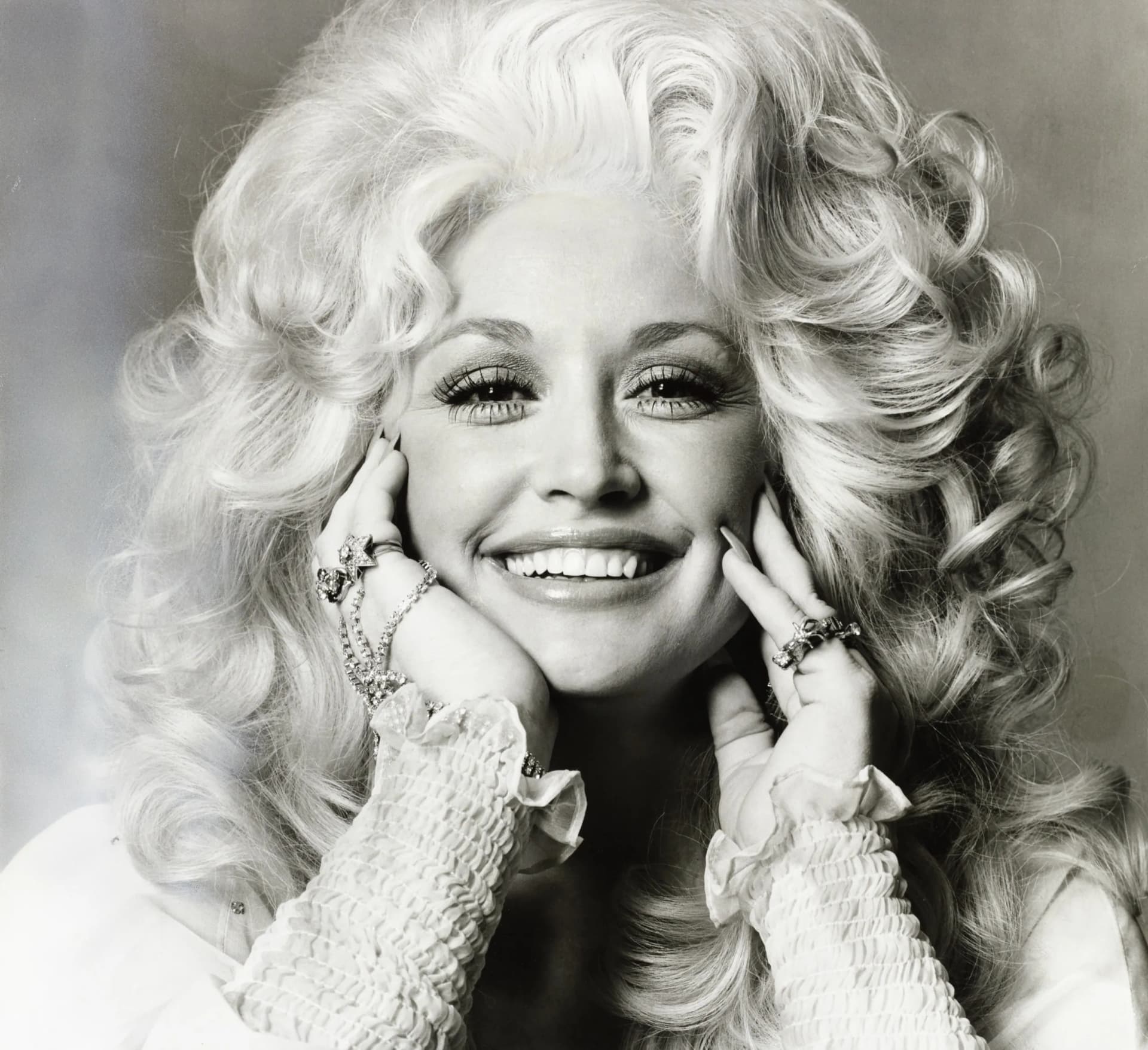 Black and white studio portrait of Dolly Parton resting her chin on her hands.