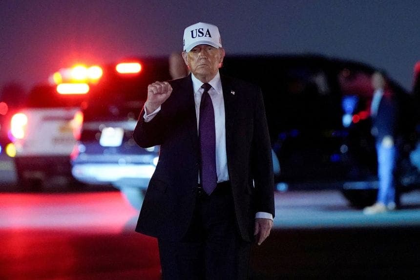 President Donald Trump pumping his fist beside a vehicle at night after disembarking Air Force One.
