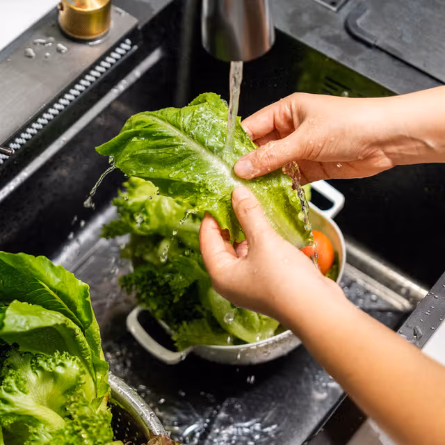 Hands rinsing a head of green lettuce under a running tap.