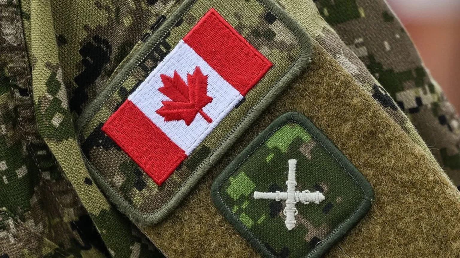 Close-up of a camouflage military uniform sleeve with a Canadian flag patch and a dark green insignia patch.