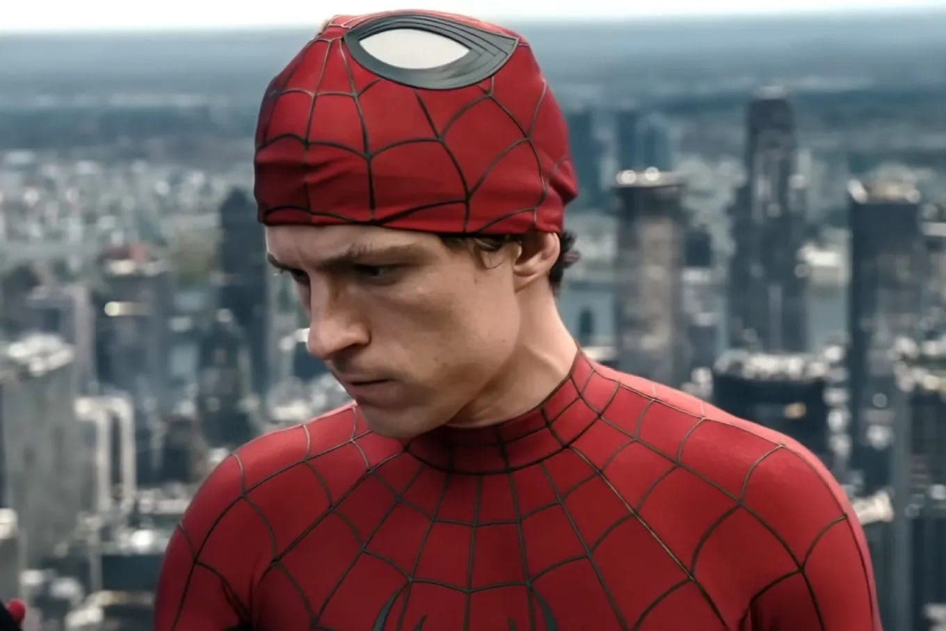 Spider-Man in a makeshift red mask standing on a rooftop above a city skyline.