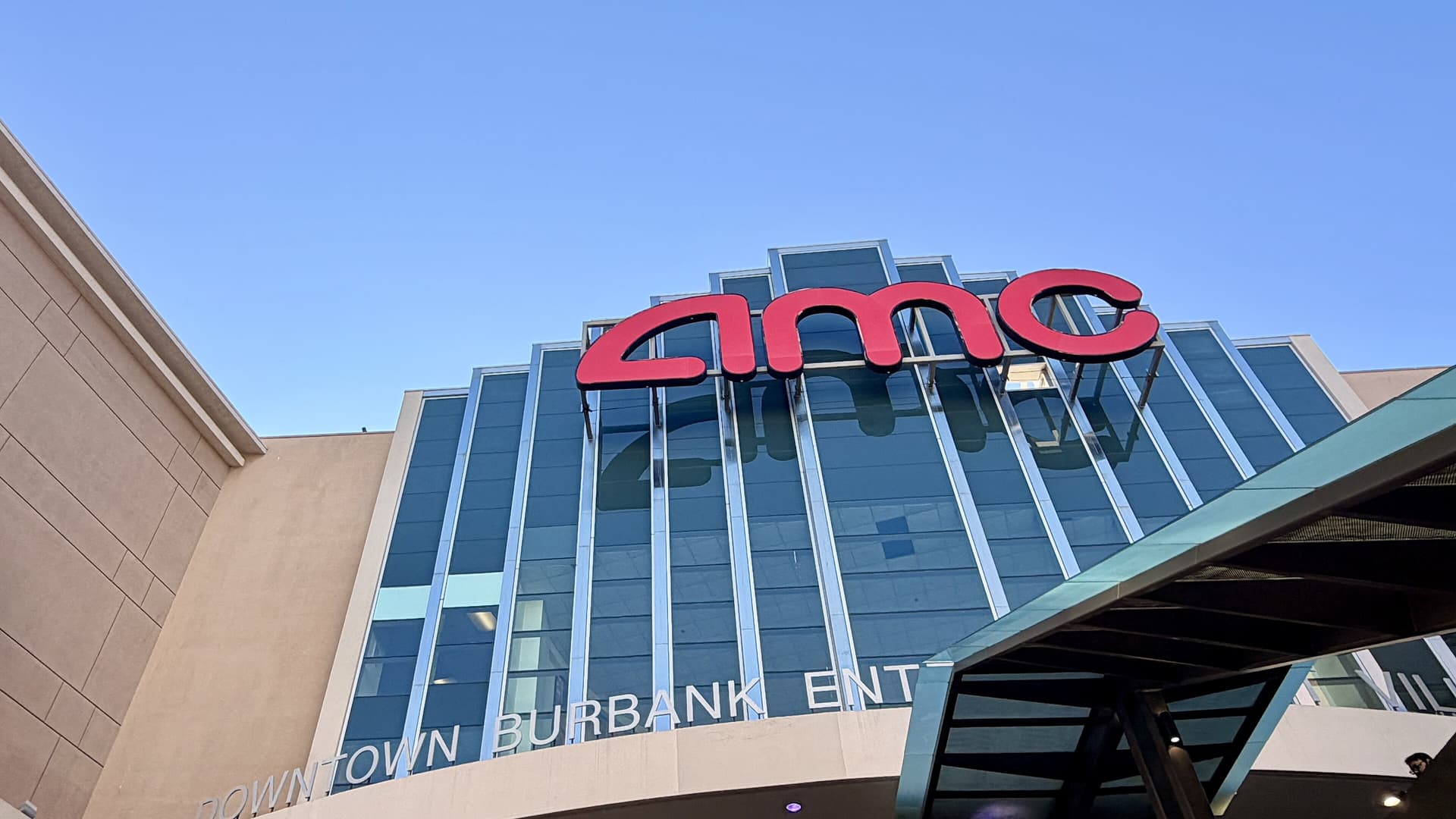 The glass-fronted AMC Burbank 16 multiplex with a large red AMC sign against a clear blue sky, seen from below.