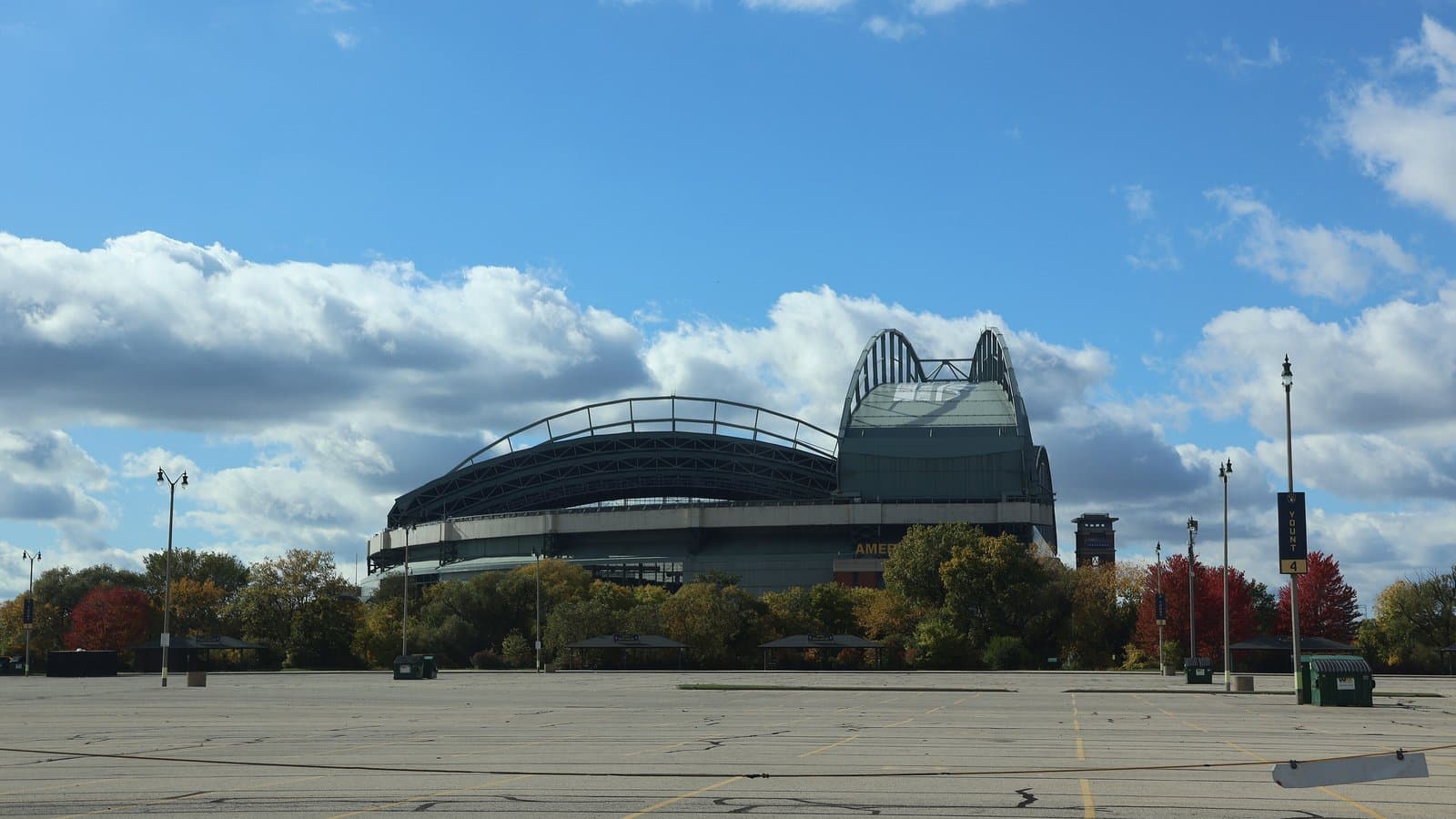 Exterior of American Family Field in Milwaukee with its fan-shaped retractable roof under a blue sky with clouds and autumn trees.