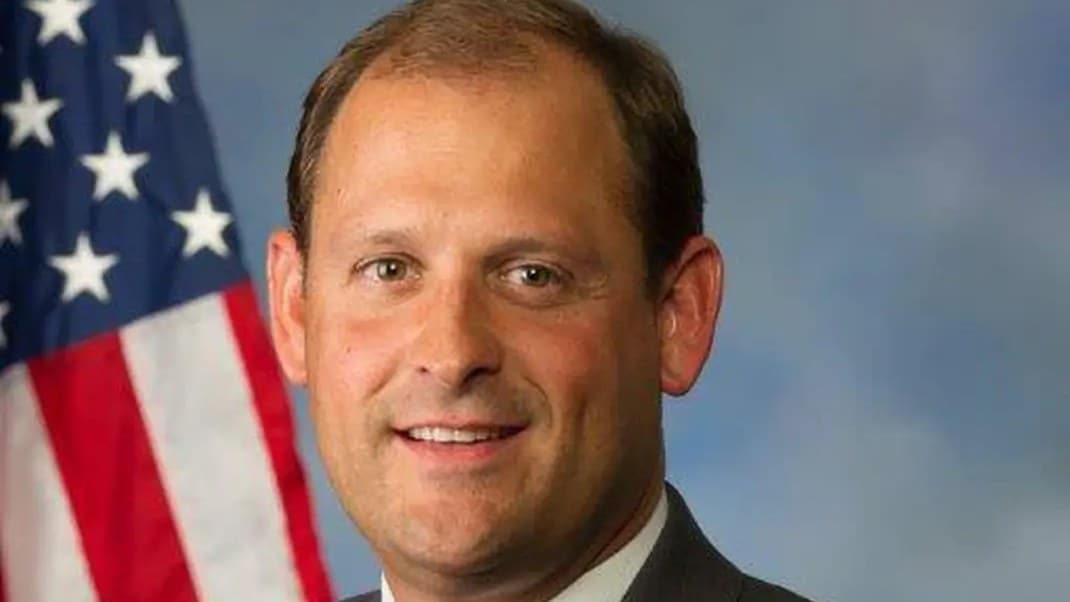 Official portrait of Rep. Andy Barr, smiling, in a dark suit in front of an American flag.