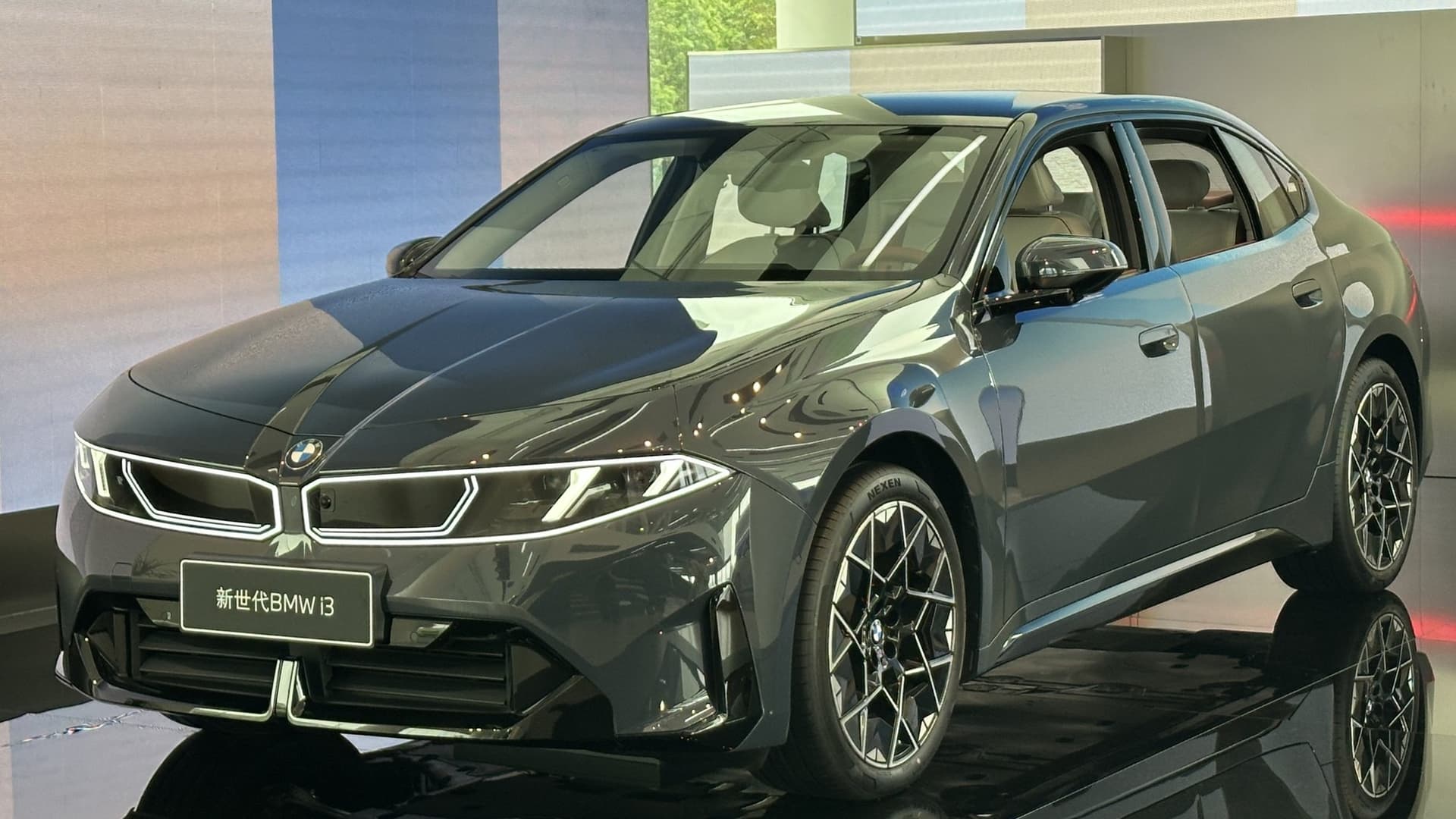 A dark grey new-generation BMW i3 electric sedan with illuminated kidney grille on a glossy display stand, with a sign reading 新世代BMW i3.