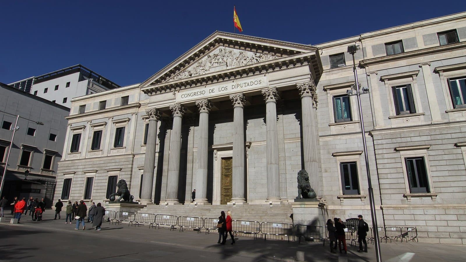 The neoclassical facade of Spain's Congress of Deputies in Madrid, with six columns, a triangular pediment and bronze lions beside the steps.