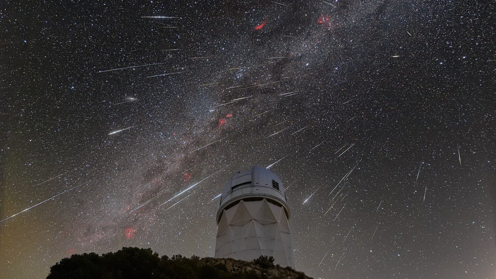 Dozens of Geminid meteor streaks radiating across a starry sky and the Milky Way above a white observatory dome on a dark ridge.