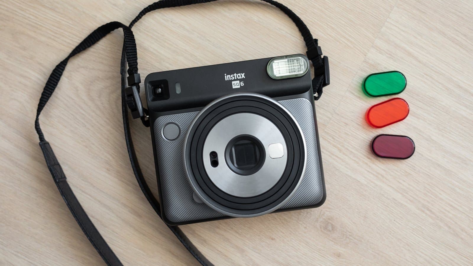 A Fujifilm Instax SQ6 square-format instant camera with a round lens barrel and flash, photographed on a plain background.