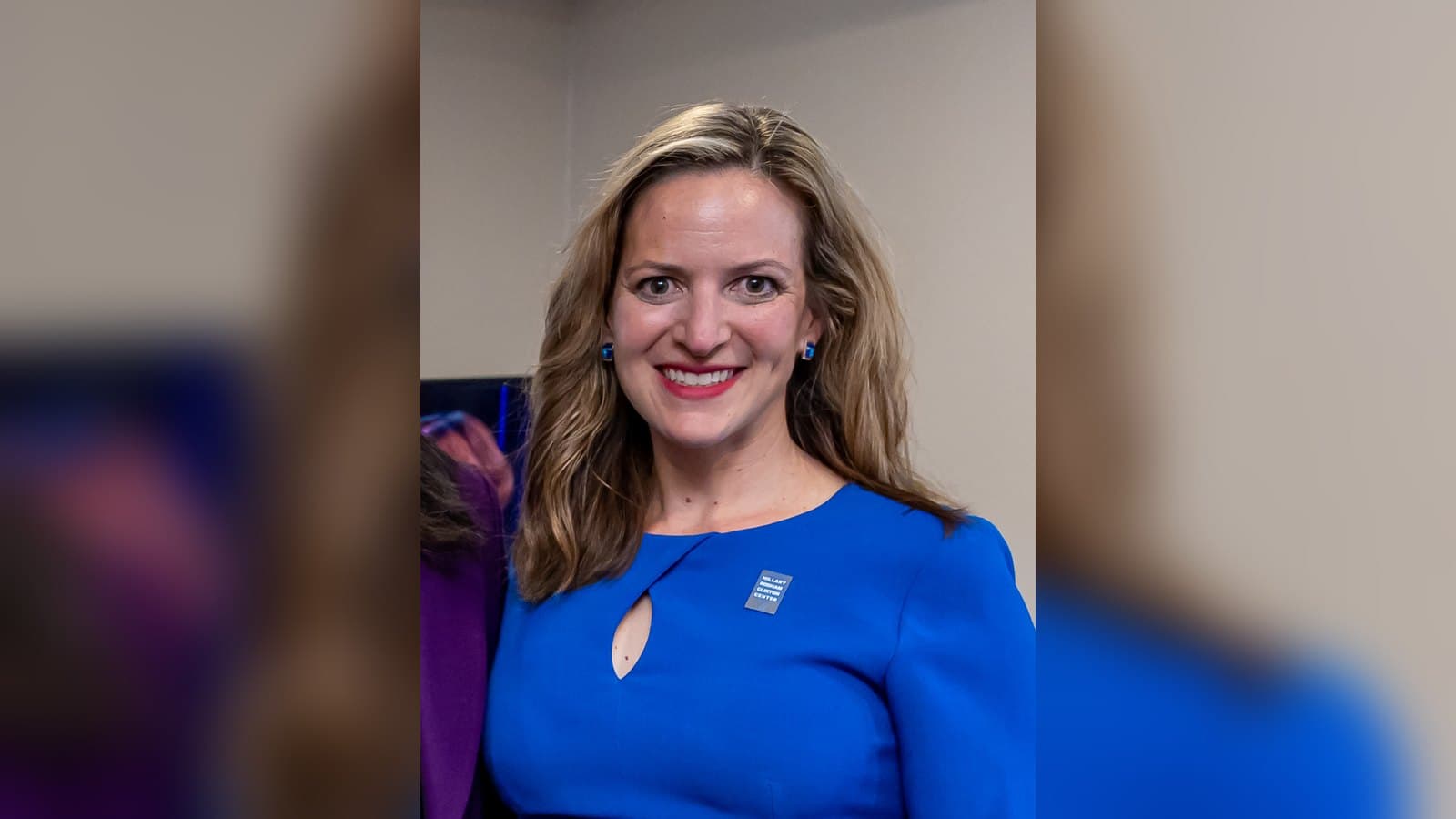 Michigan Secretary of State Jocelyn Benson, with long hair and a blue dress, smiles at an event.