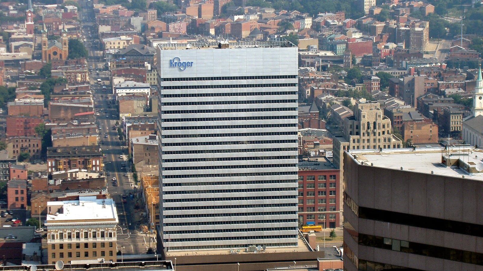 Aerial view of downtown Cincinnati with Kroger's tall white corporate headquarters tower, its blue Kroger logo near the top, surrounded by brick buildings and streets.