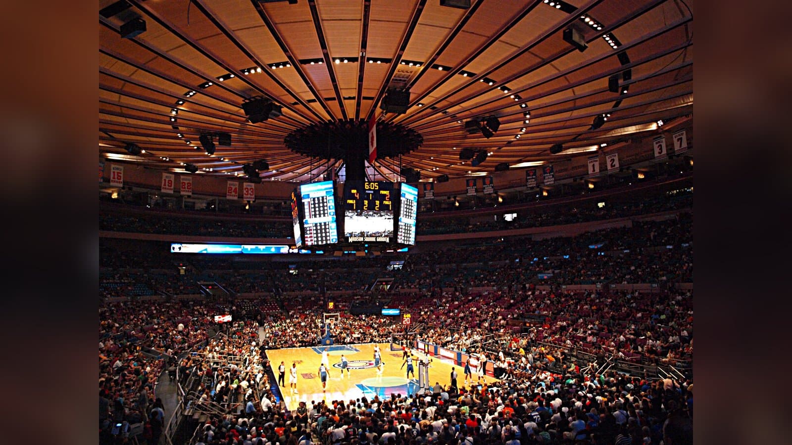 Packed crowd inside Madison Square Garden looking down at the basketball court beneath the arena's circular ceiling and center-hung scoreboard.