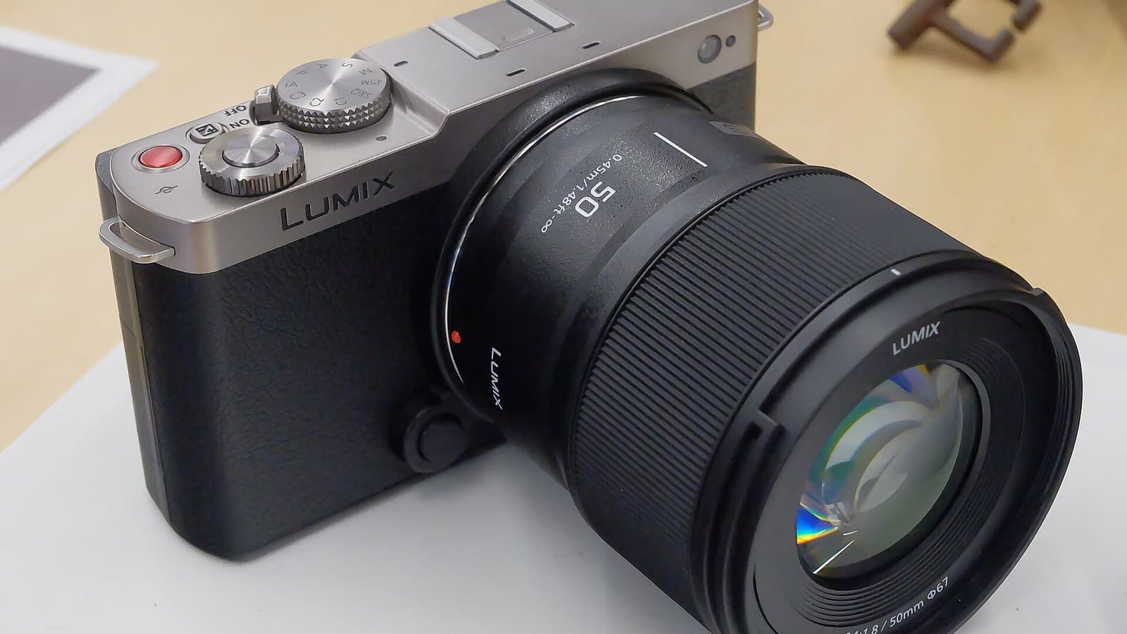 A silver and gray Panasonic Lumix S9 compact full-frame camera with a black Lumix 50mm prime lens, on a white table.