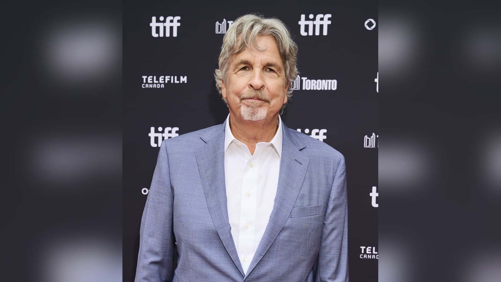 Director Peter Farrelly, grey-haired in a light blue suit and white shirt, on the red carpet in front of a TIFF and Telefilm Canada step-and-repeat.