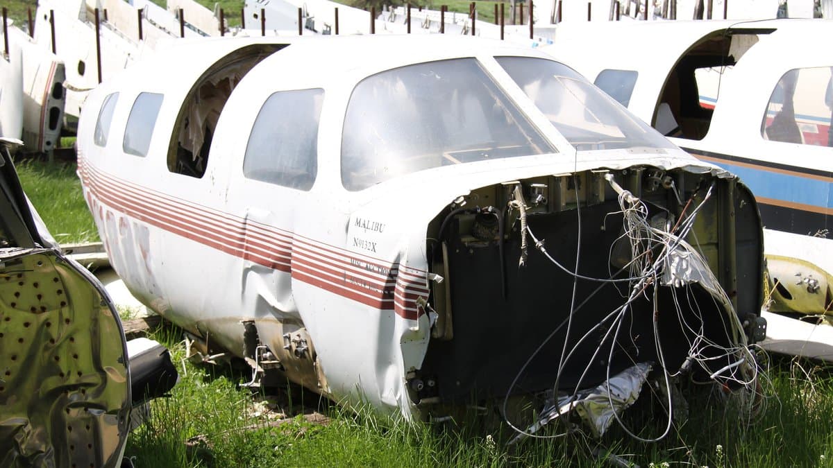 A white single-engine Piper PA-46 Malibu airplane with red and blue stripes parked on an airport ramp.