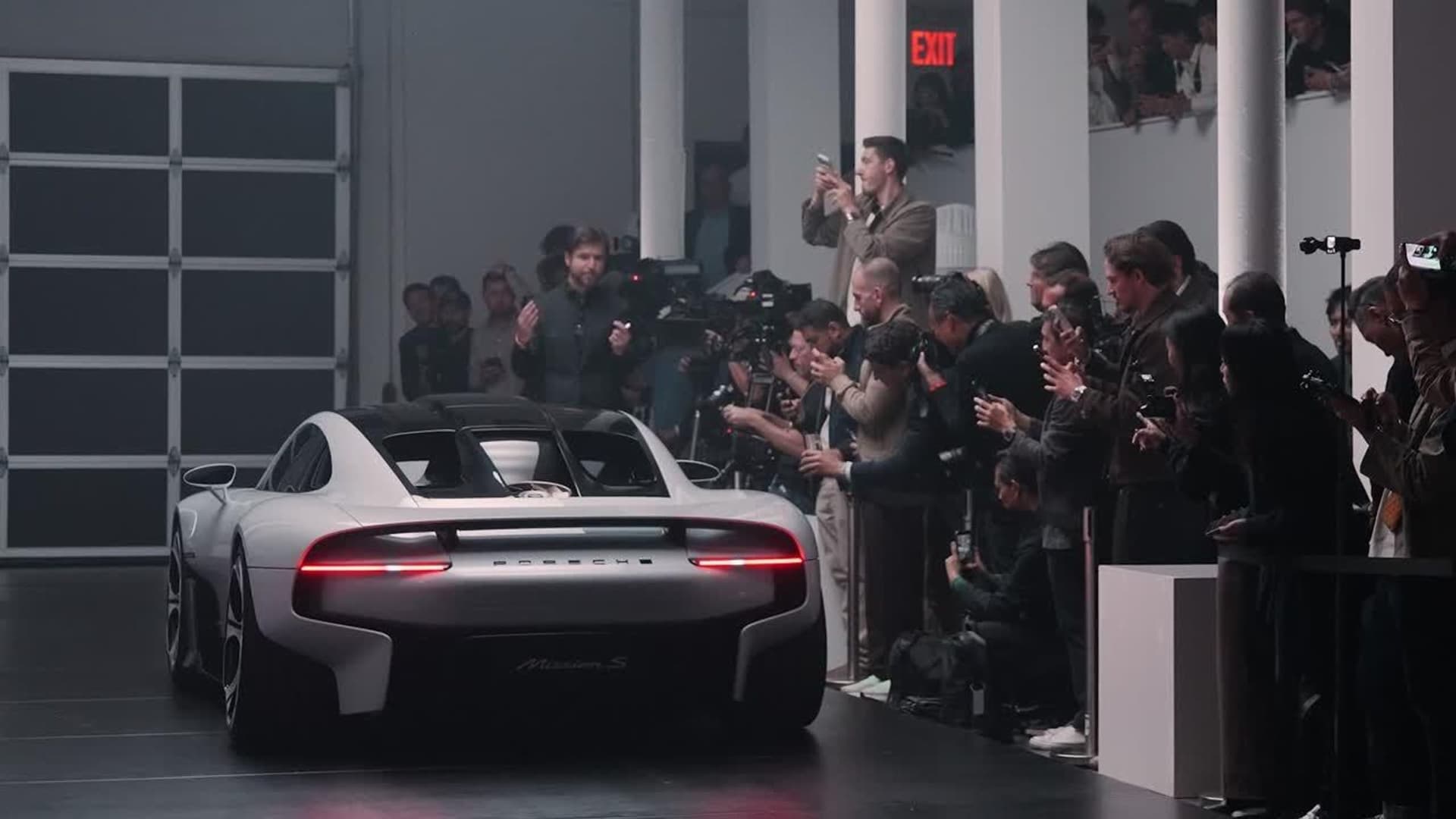 Rear view of the white and black Porsche Mission S concept with a full-width red light bar, surrounded by photographers and guests at its New York reveal.