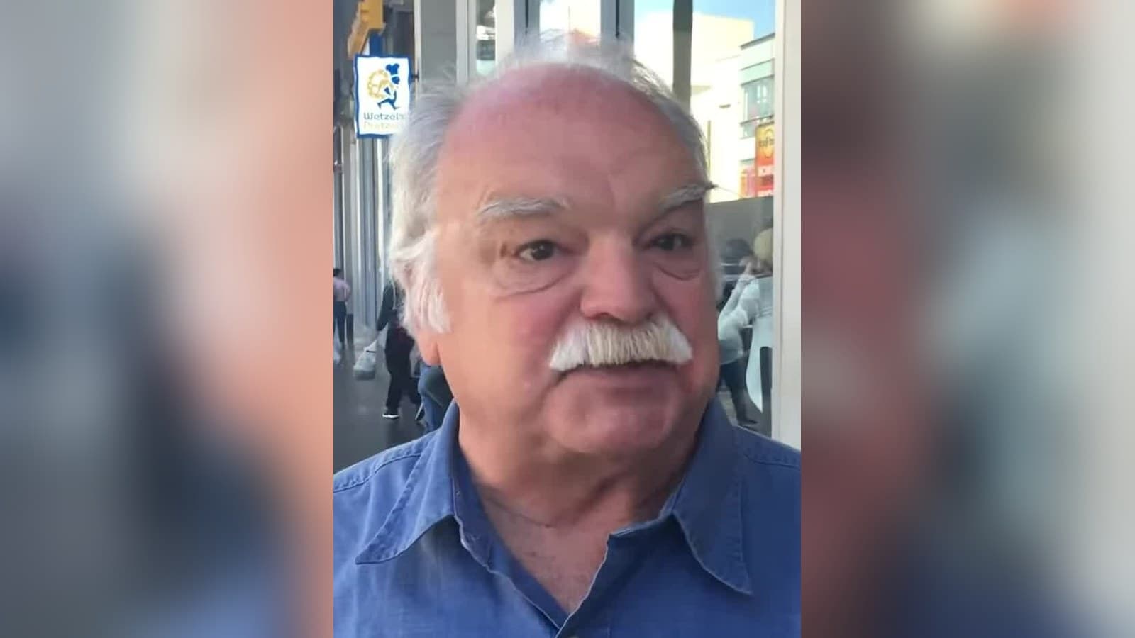 Richard Riehle, a white-haired actor with a gray mustache in a blue denim shirt, speaking on a Los Angeles street in 2016