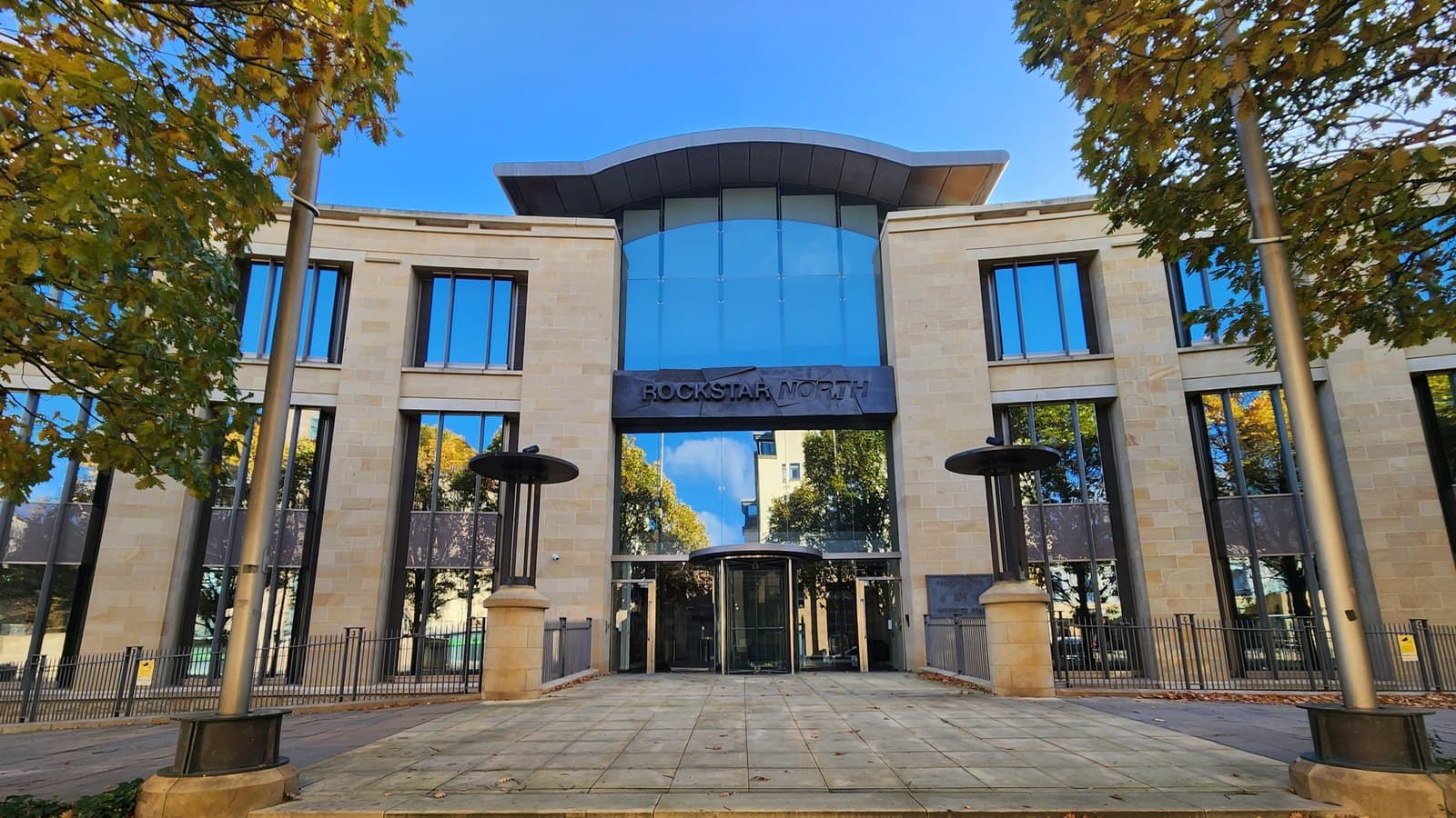 The stone and glass front entrance of the Rockstar North studio building in Edinburgh under a blue sky, with the Rockstar North sign above a revolving door.
