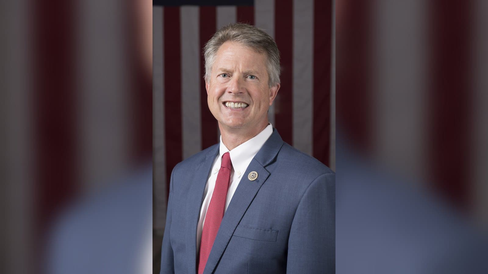 Official portrait of Roger Marshall in a blue suit and red tie, smiling in front of an American flag.