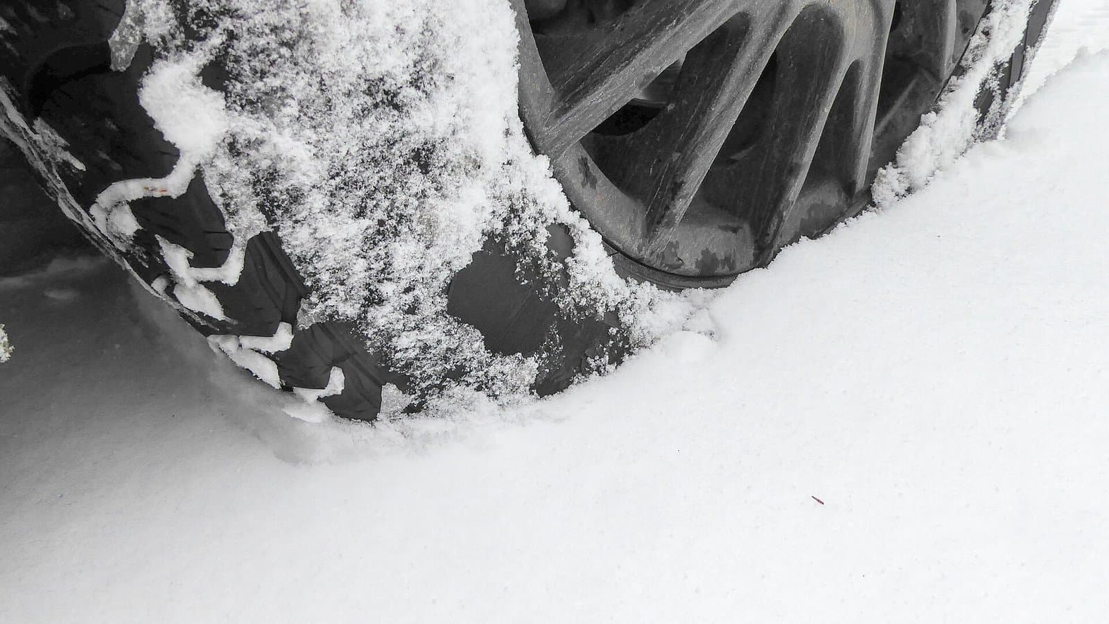 Close-up of a car's winter tire and wheel rolling through fresh powdery snow.