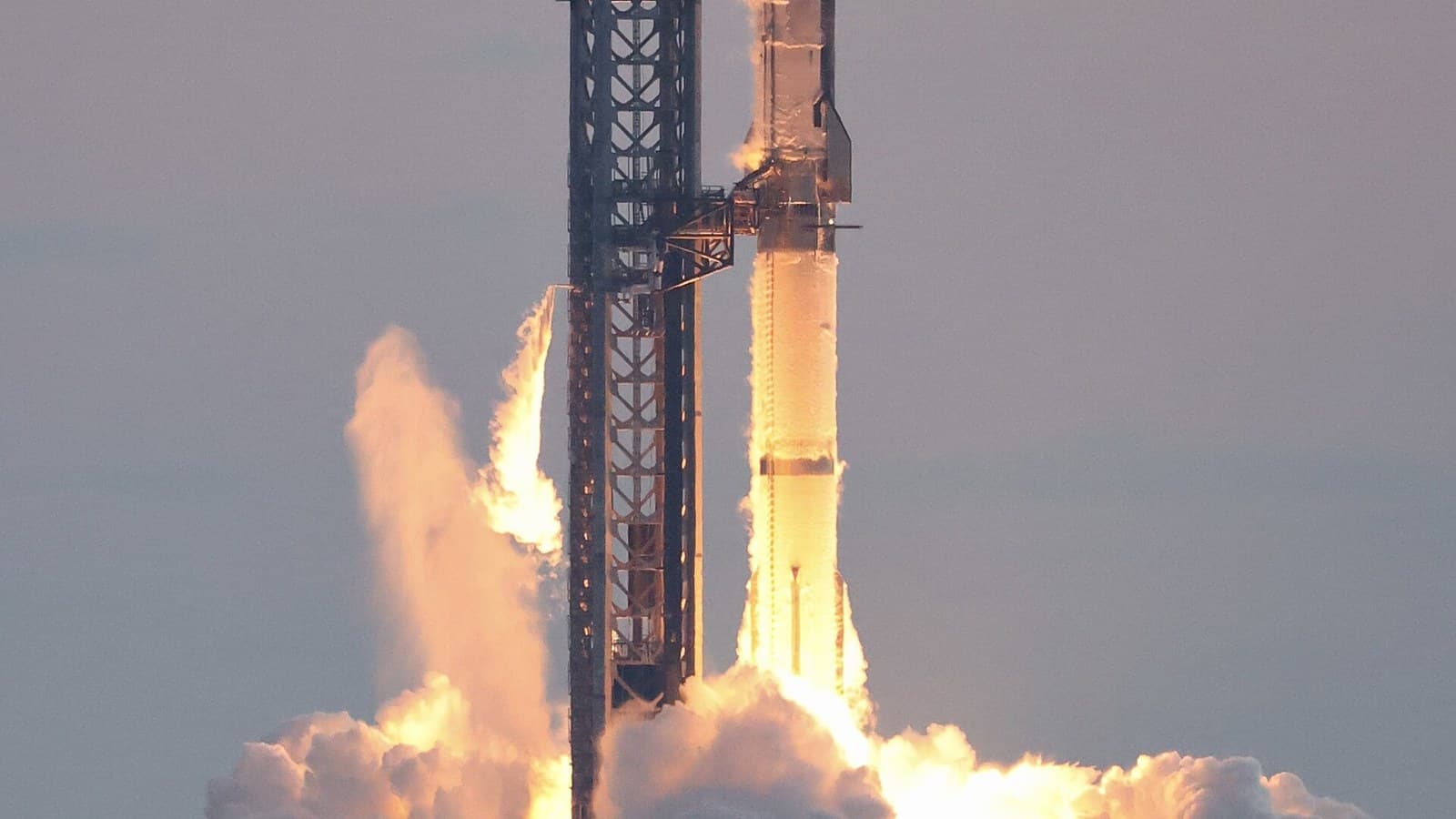 SpaceX's stainless-steel Starship rocket lifting off beside its launch tower in a cloud of fire and steam
