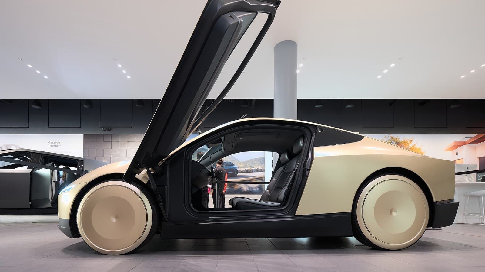 A gold two-seat Tesla Cybercab with its butterfly door raised, shown in profile inside a bright Tesla showroom