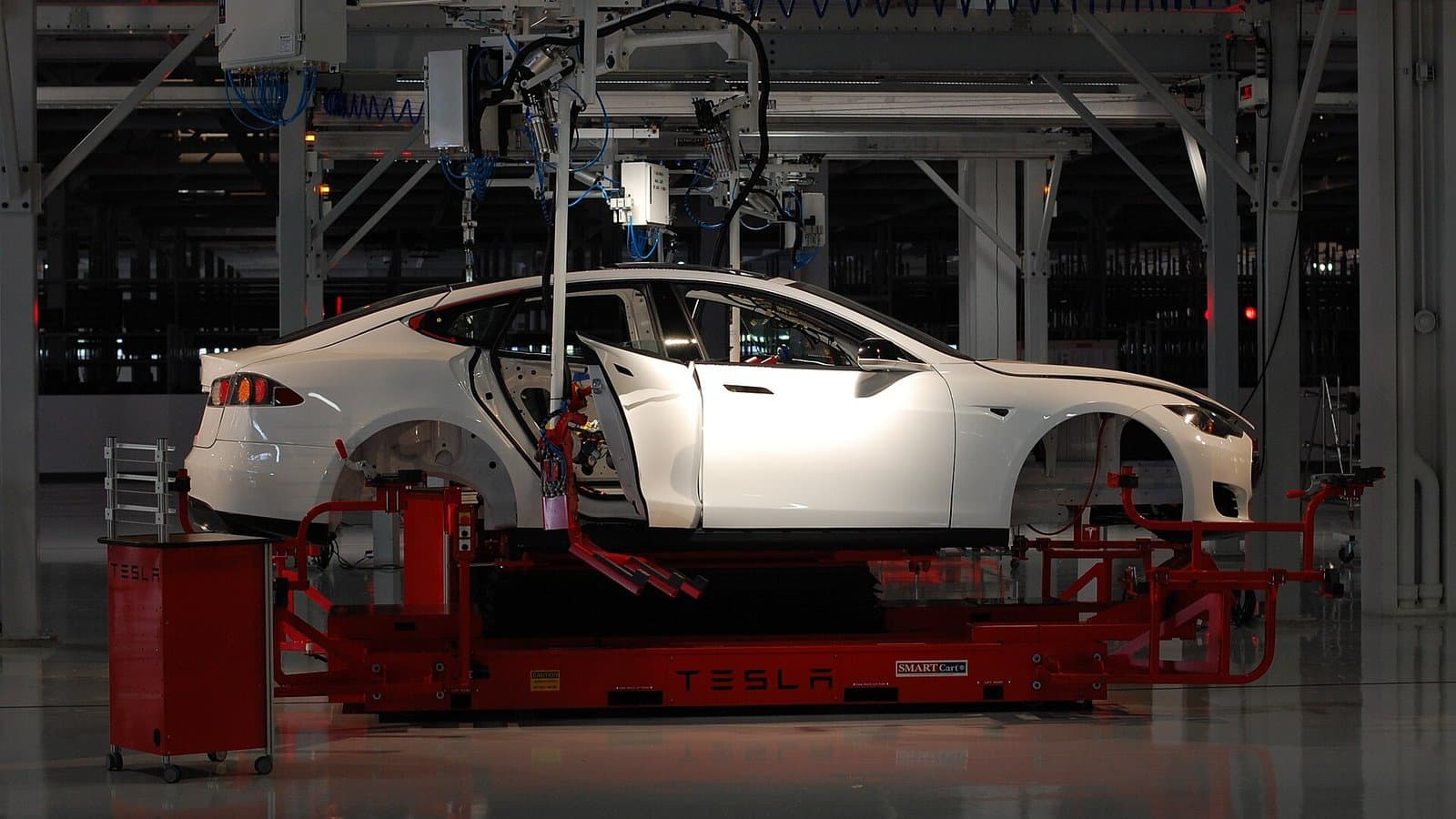 A white Tesla car body suspended on red robotic assembly equipment inside the Tesla factory in Fremont, California.
