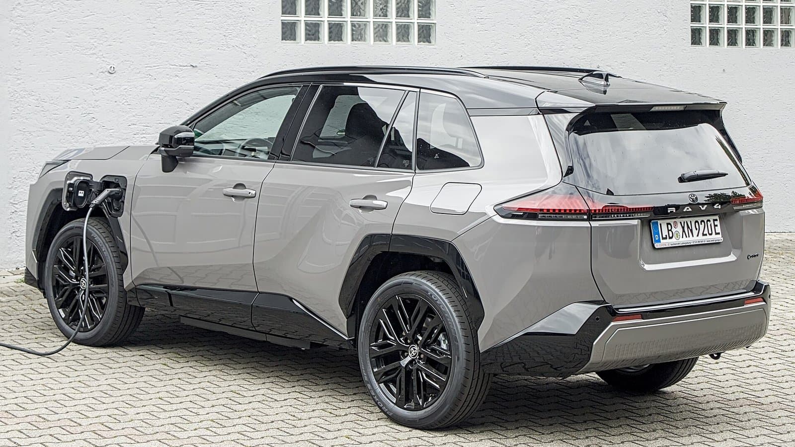 A silver new-generation Toyota RAV4 plug-in hybrid SUV parked with a charging cable plugged into its rear side.
