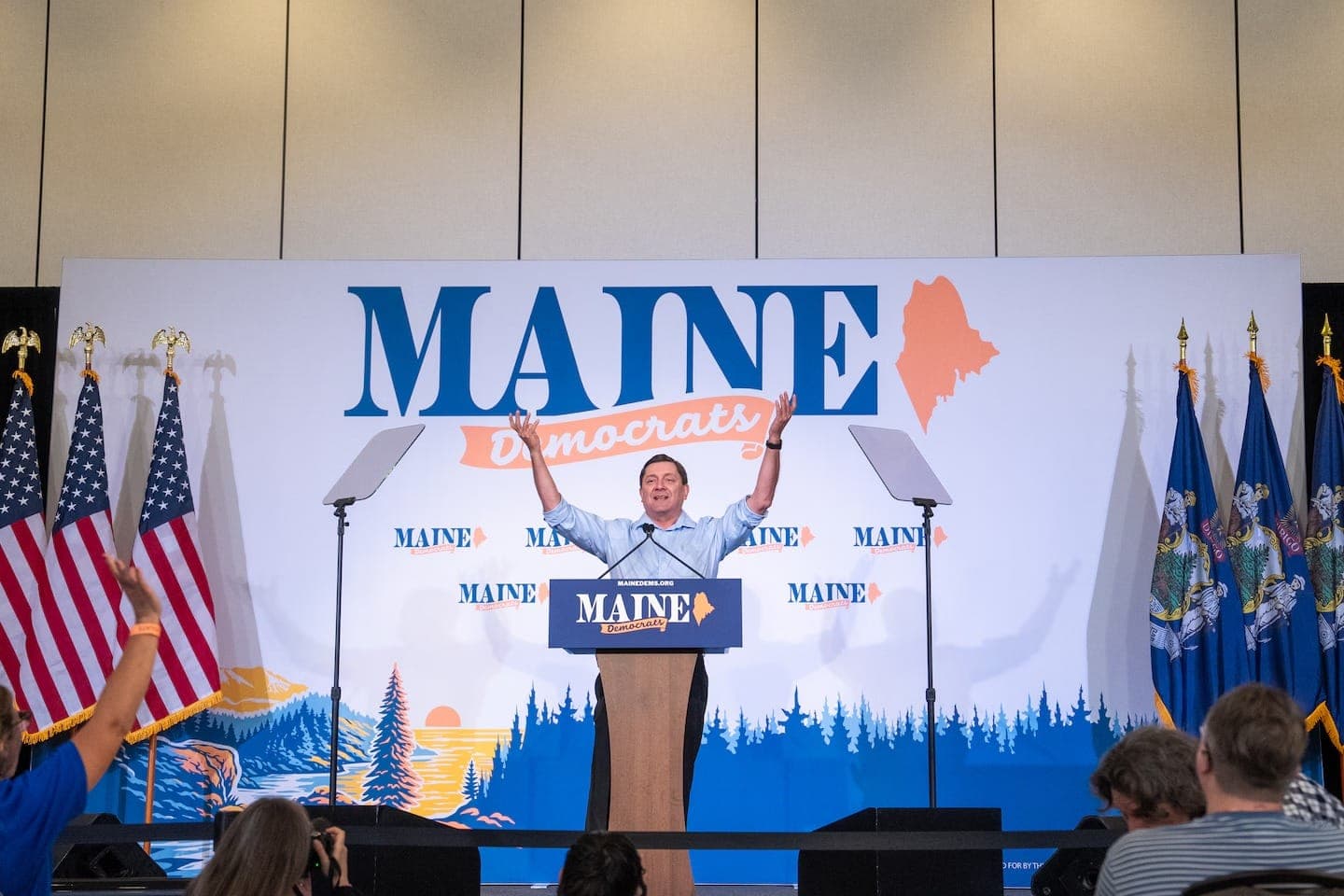Troy Jackson raises his arms on stage at the Maine Democrats convention in Bangor.