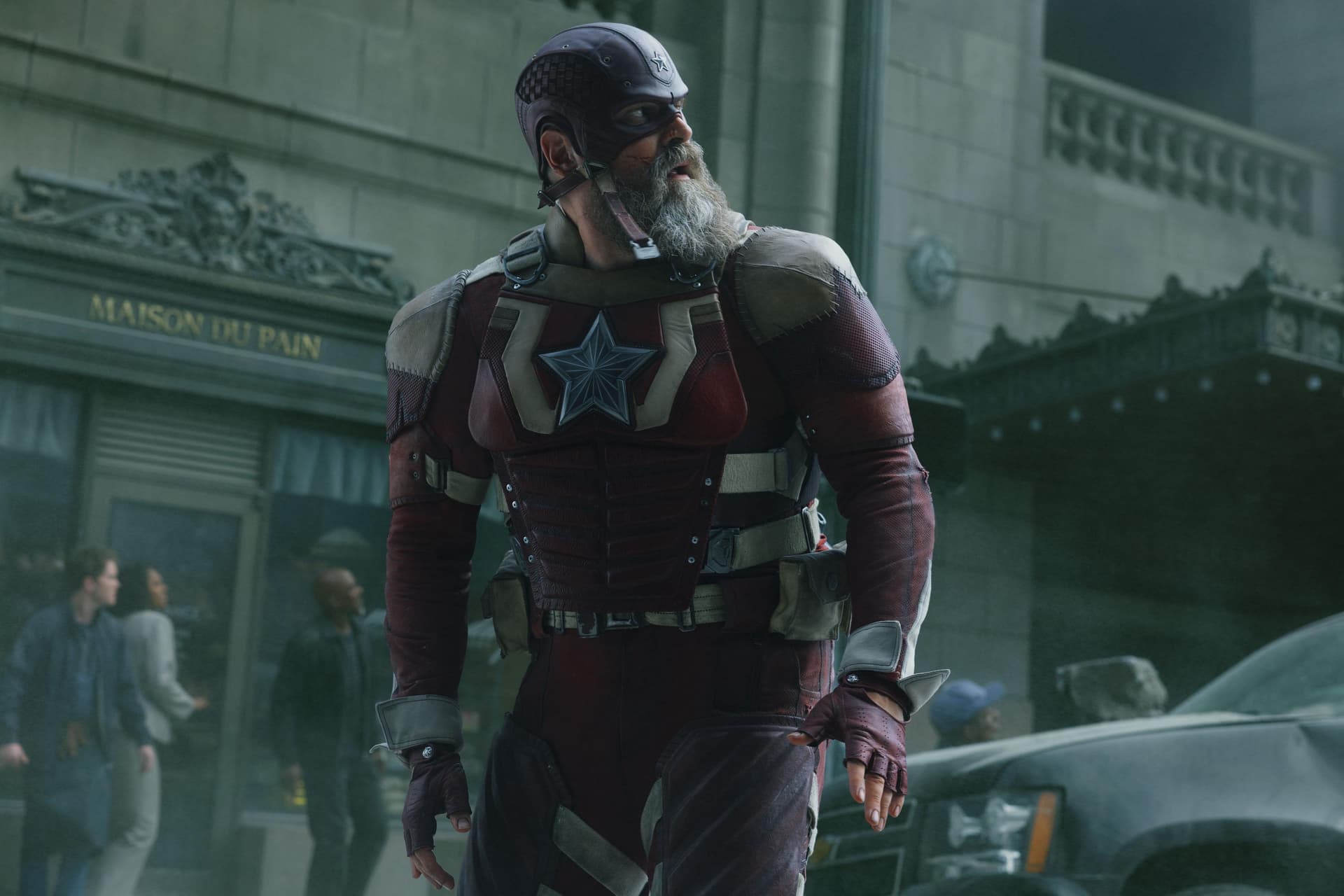 David Harbour in costume as the Red Guardian, in a red suit with a white star, standing on a city street.