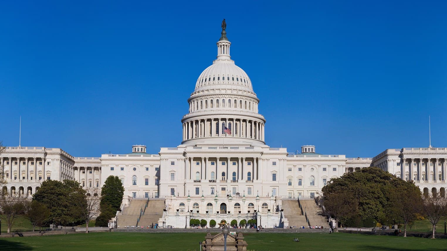The U.S. Capitol building with its white dome under a clear blue sky, seen across the West Lawn.