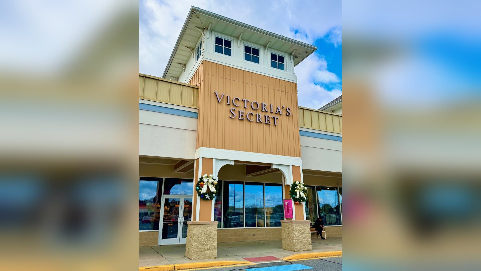 Exterior of a Victoria's Secret store with the brand name in large letters on a tan tower above an arched entrance flanked by holiday wreaths.