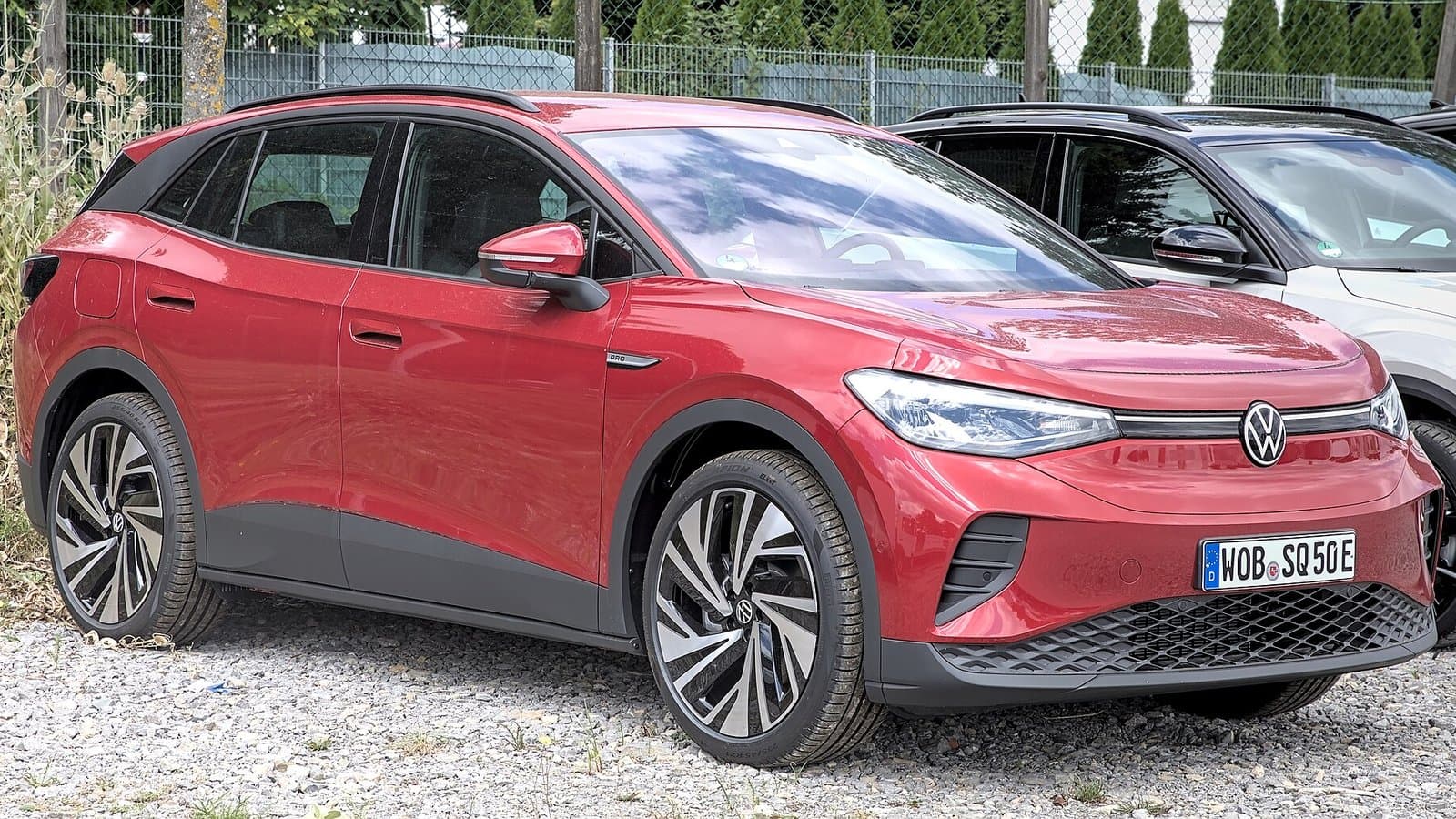 A red Volkswagen ID.4 electric compact SUV parked on gravel, seen from the front left.