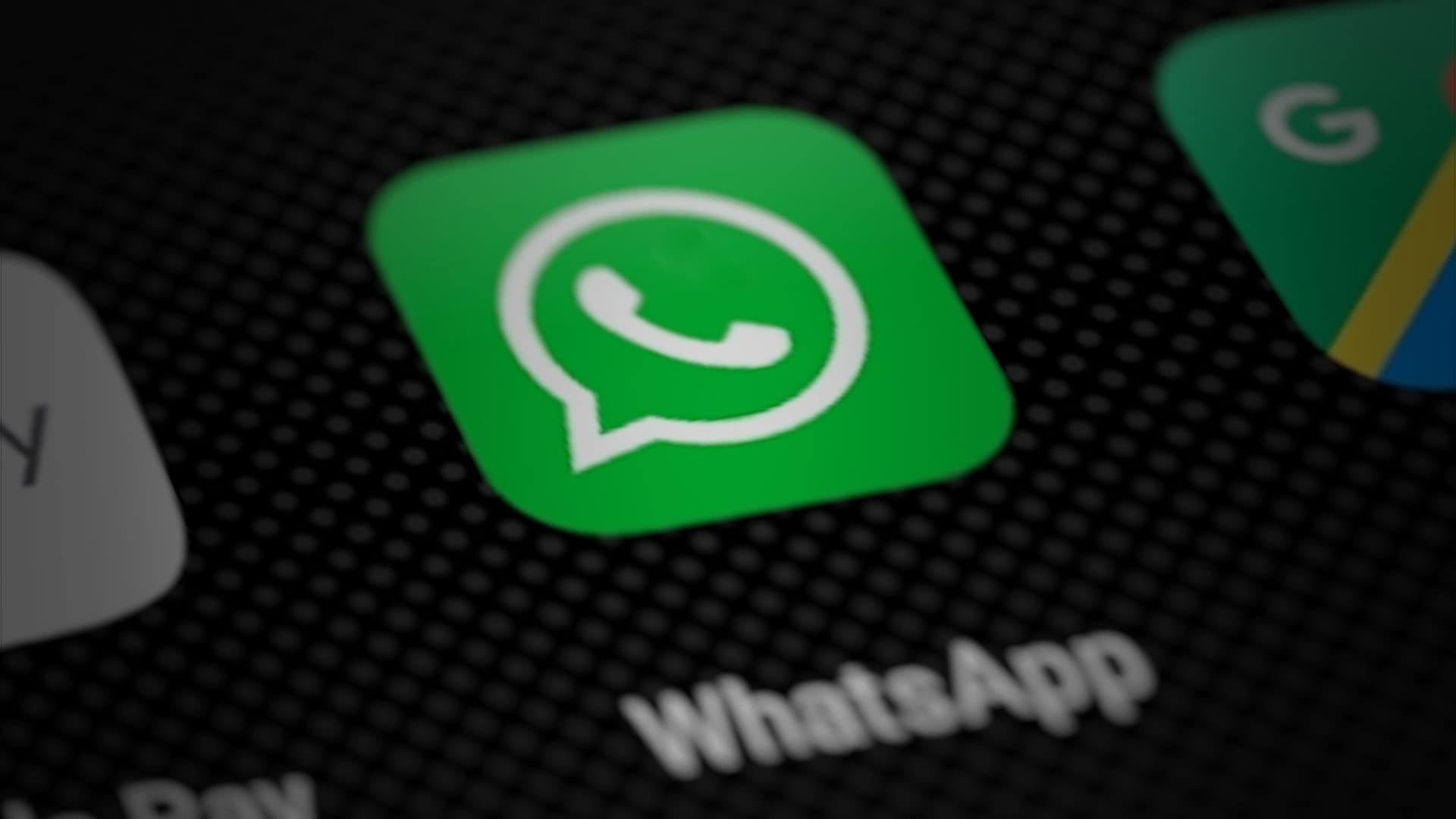 Close-up of the green WhatsApp app icon with its white phone-in-speech-bubble logo on a dark smartphone home screen, next to other app icons.