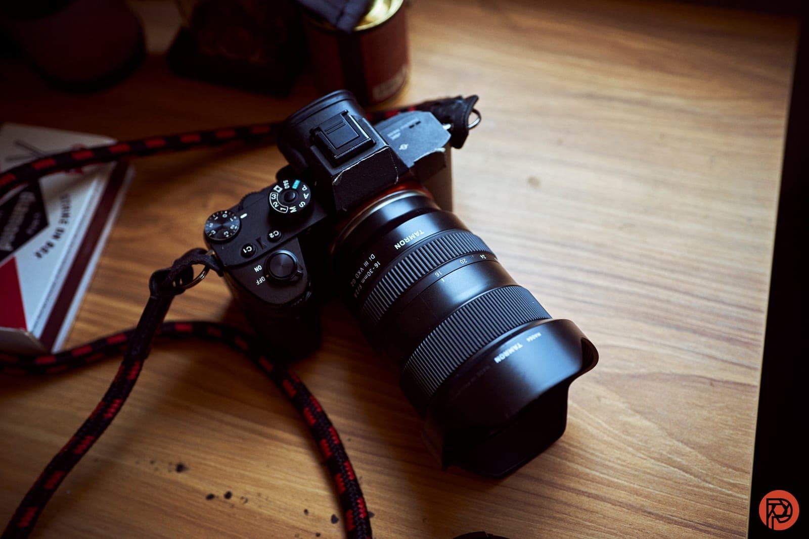 A mirrorless camera fitted with a Tamron zoom lens, resting on a wooden floor.