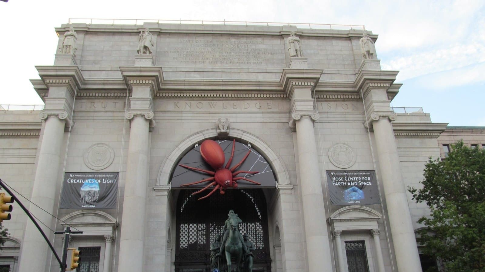 The columned stone entrance of the American Museum of Natural History in New York, with a bronze equestrian statue in front and banners hanging on the facade.