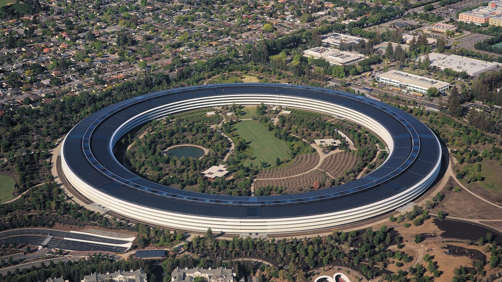 Aerial view of Apple Park in Cupertino, the ring-shaped Apple headquarters building surrounded by trees and a central garden.