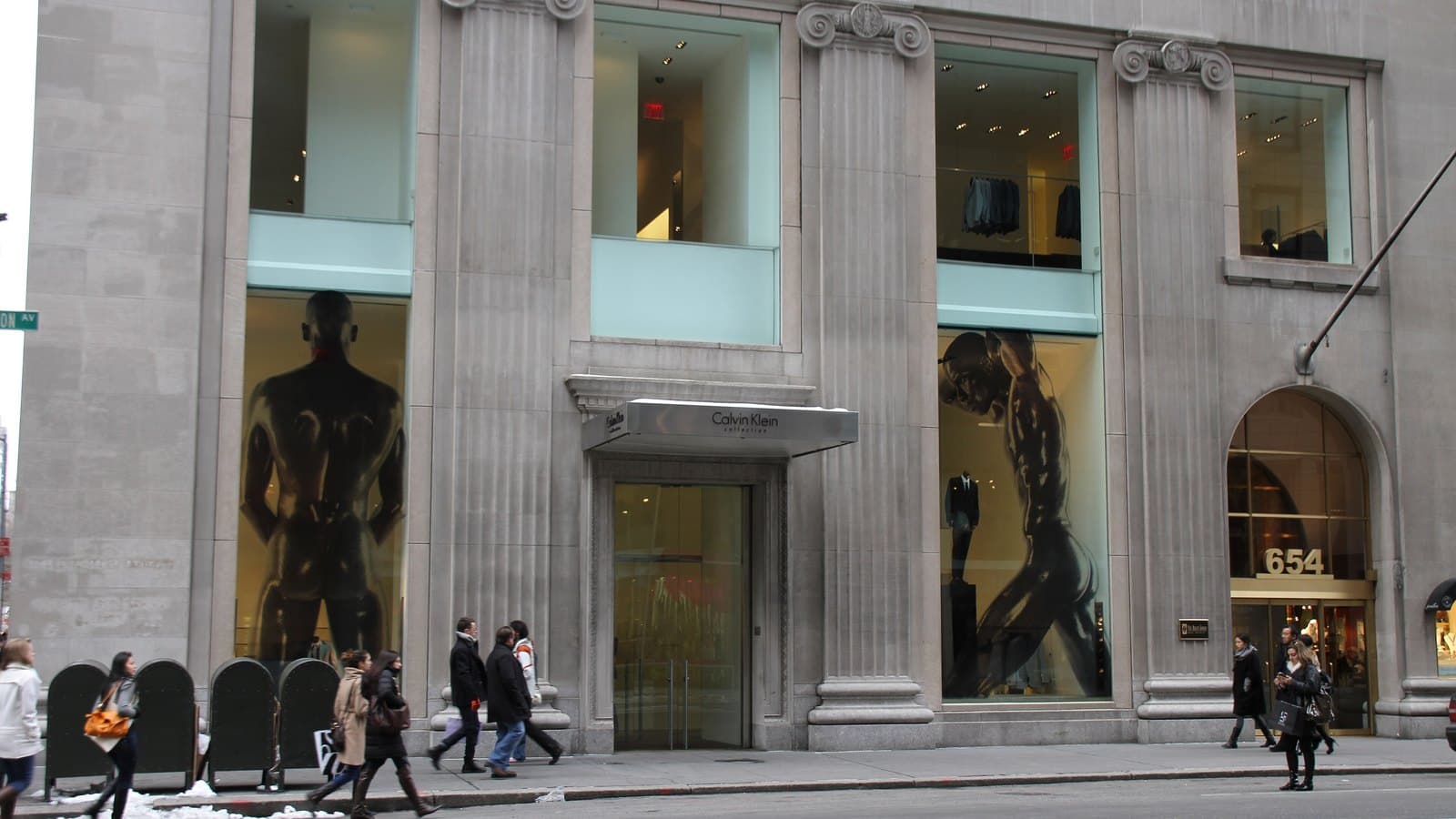 The grey stone facade of the Calvin Klein Collection store at 654 Madison Avenue in New York, with tall display windows and pedestrians on the sidewalk.