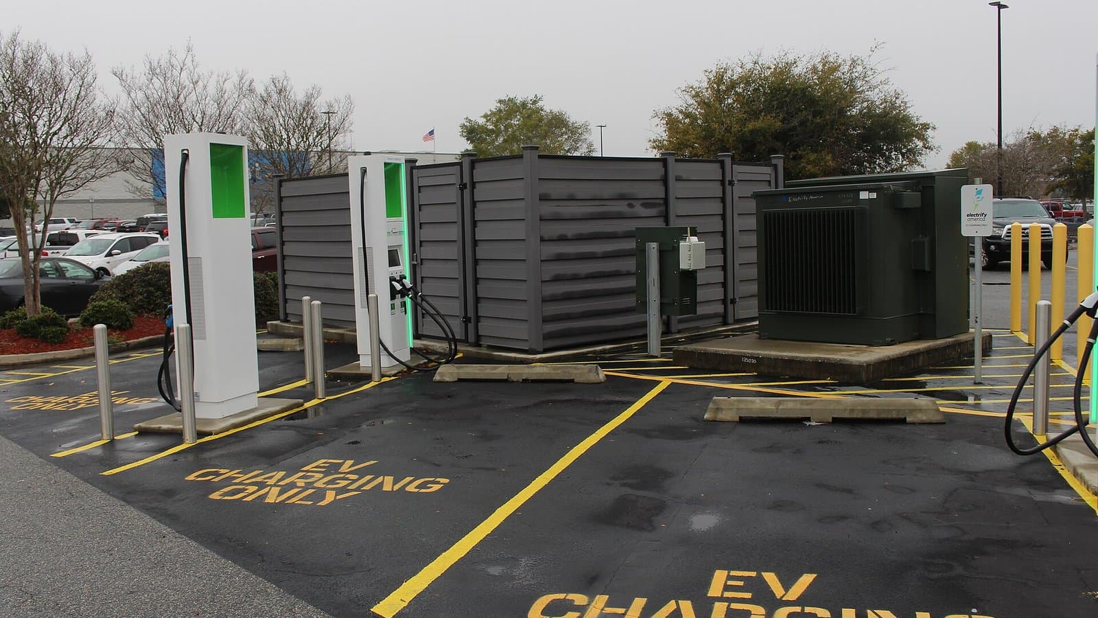 Electric vehicle fast chargers in a parking lot with yellow 'EV charging only' markings painted on the pavement.
