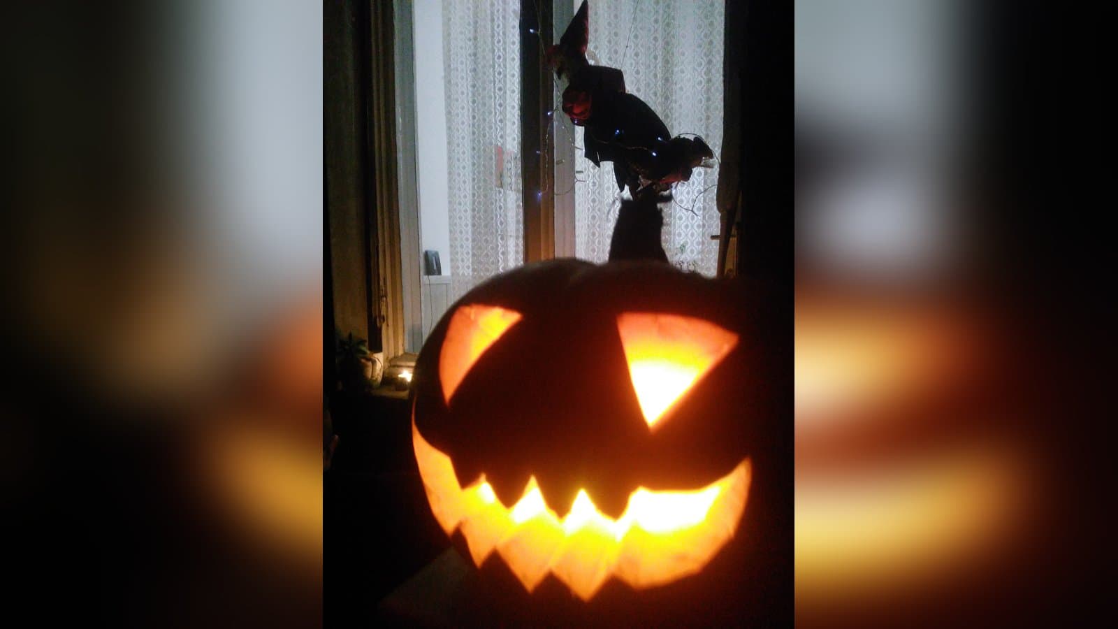 A glowing jack-o'-lantern with triangular eyes and a jagged grin, lit from inside by a candle and set in a dark window.