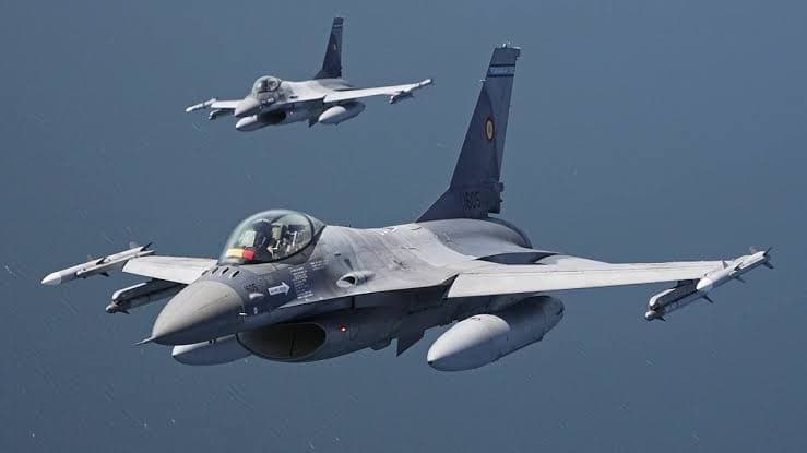 Two grey Romanian Air Force F-16 fighter jets with missiles under their wings flying low over dark blue water.