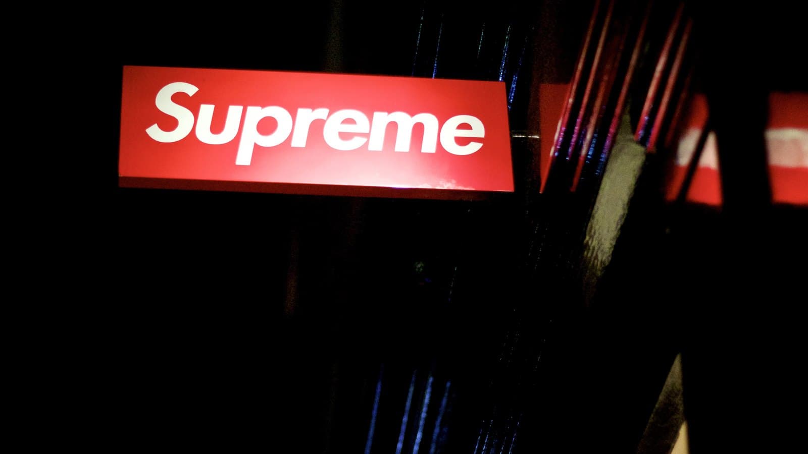 Supreme's red box logo sign glowing above a dark shopfront at night in London.