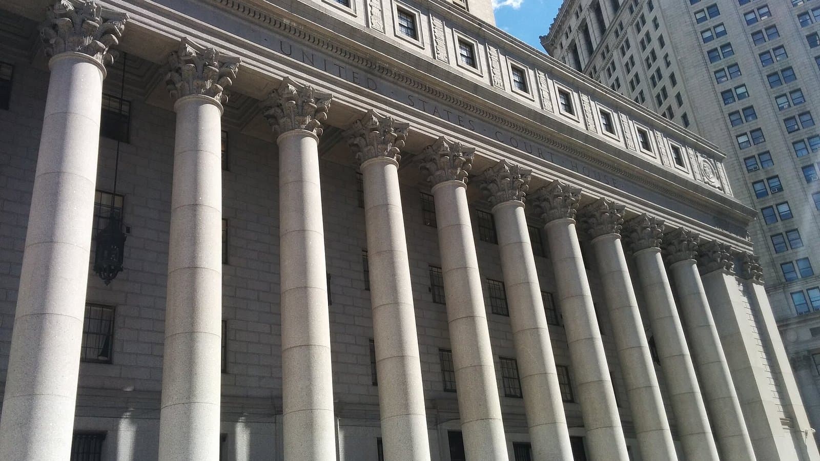Tall stone Corinthian columns on the facade of the Thurgood Marshall United States Courthouse in New York, seen from below.