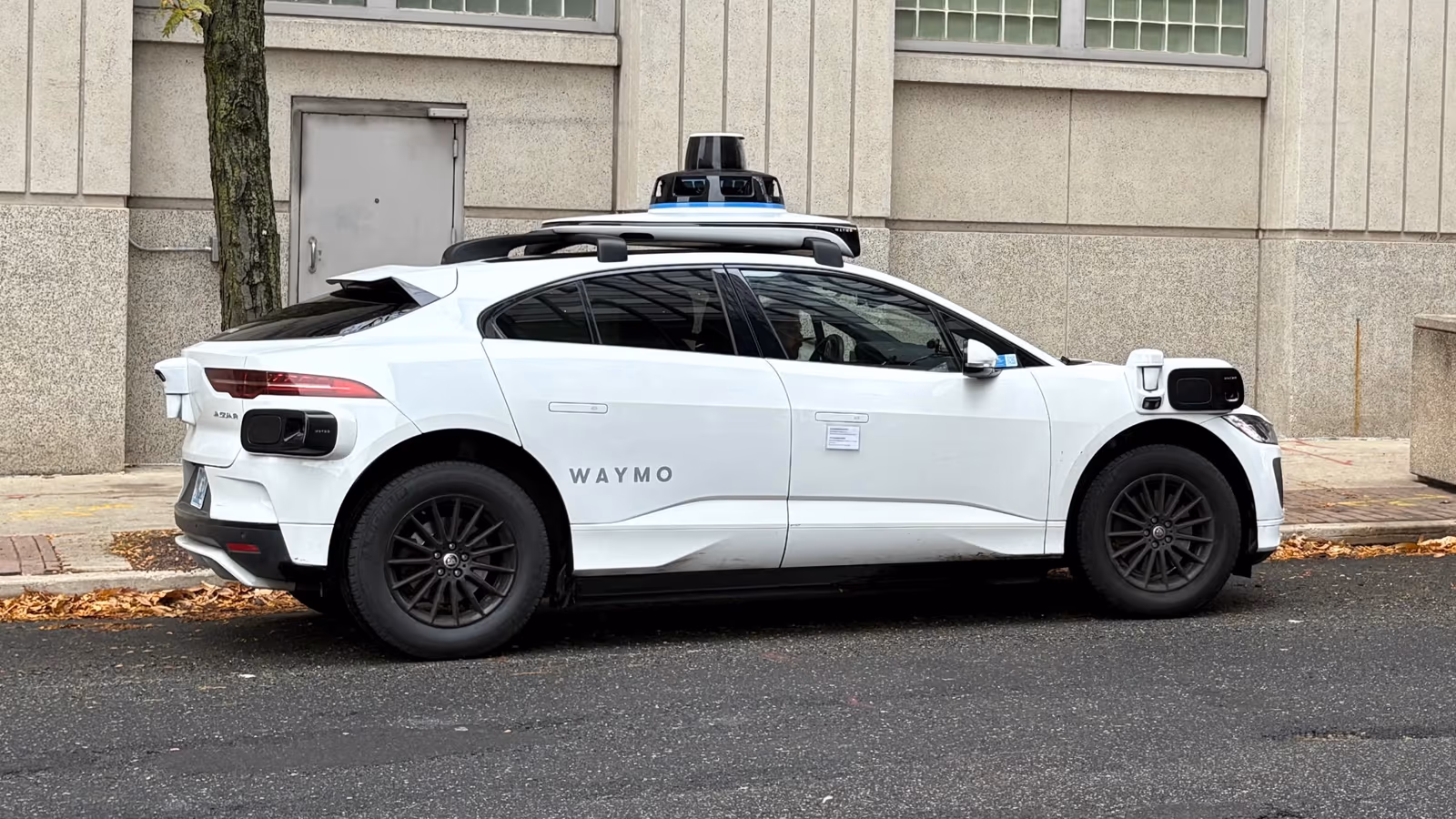 A white Waymo autonomous vehicle driving on a street in Philadelphia.