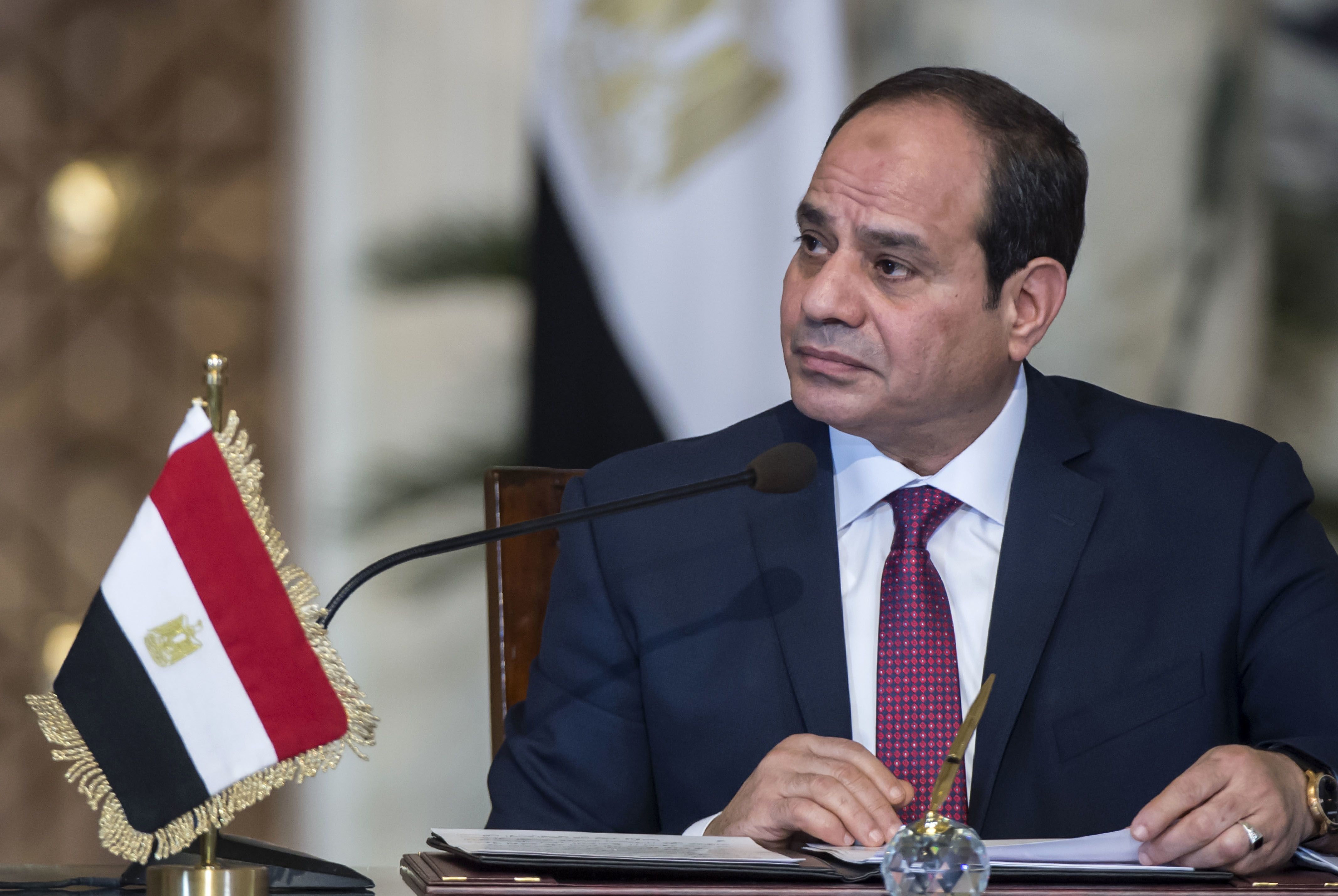 Abdel Fattah al-Sisi in a dark suit speaking at a desk with an Egyptian flag beside him.