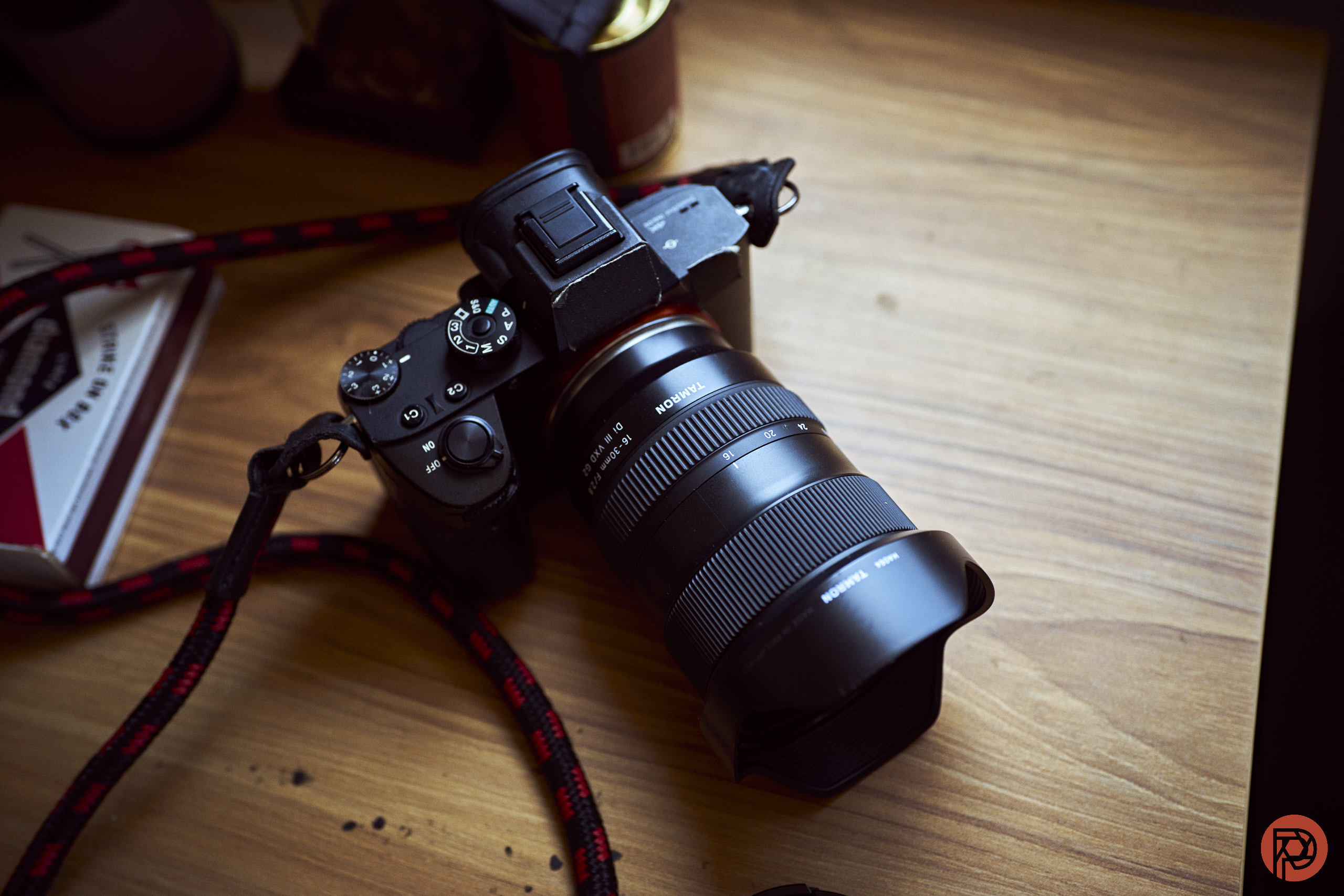 A mirrorless camera fitted with a Tamron zoom lens, resting on a wooden floor.