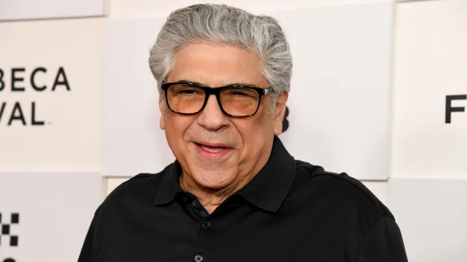 Vincent Pastore in dark-framed glasses and a black shirt, smiling at a press event.
