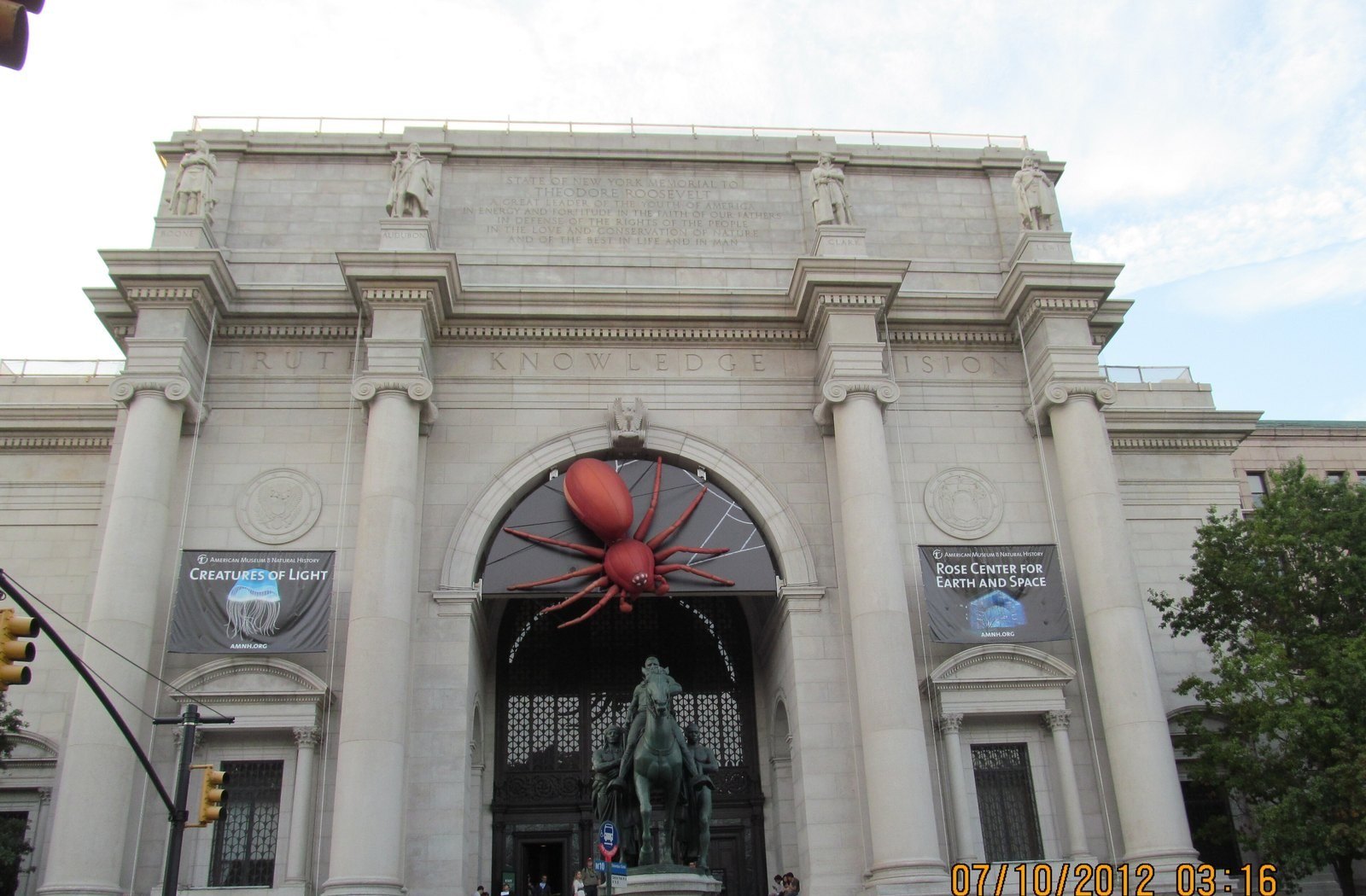 The columned stone entrance of the American Museum of Natural History in New York, with a bronze equestrian statue in front and banners hanging on the facade.