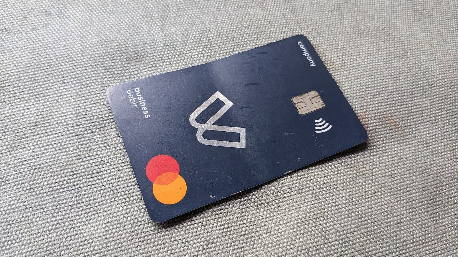 A dark blue contactless payment card with a chip and a red-and-orange Mastercard logo lying at an angle on a grey carpet.