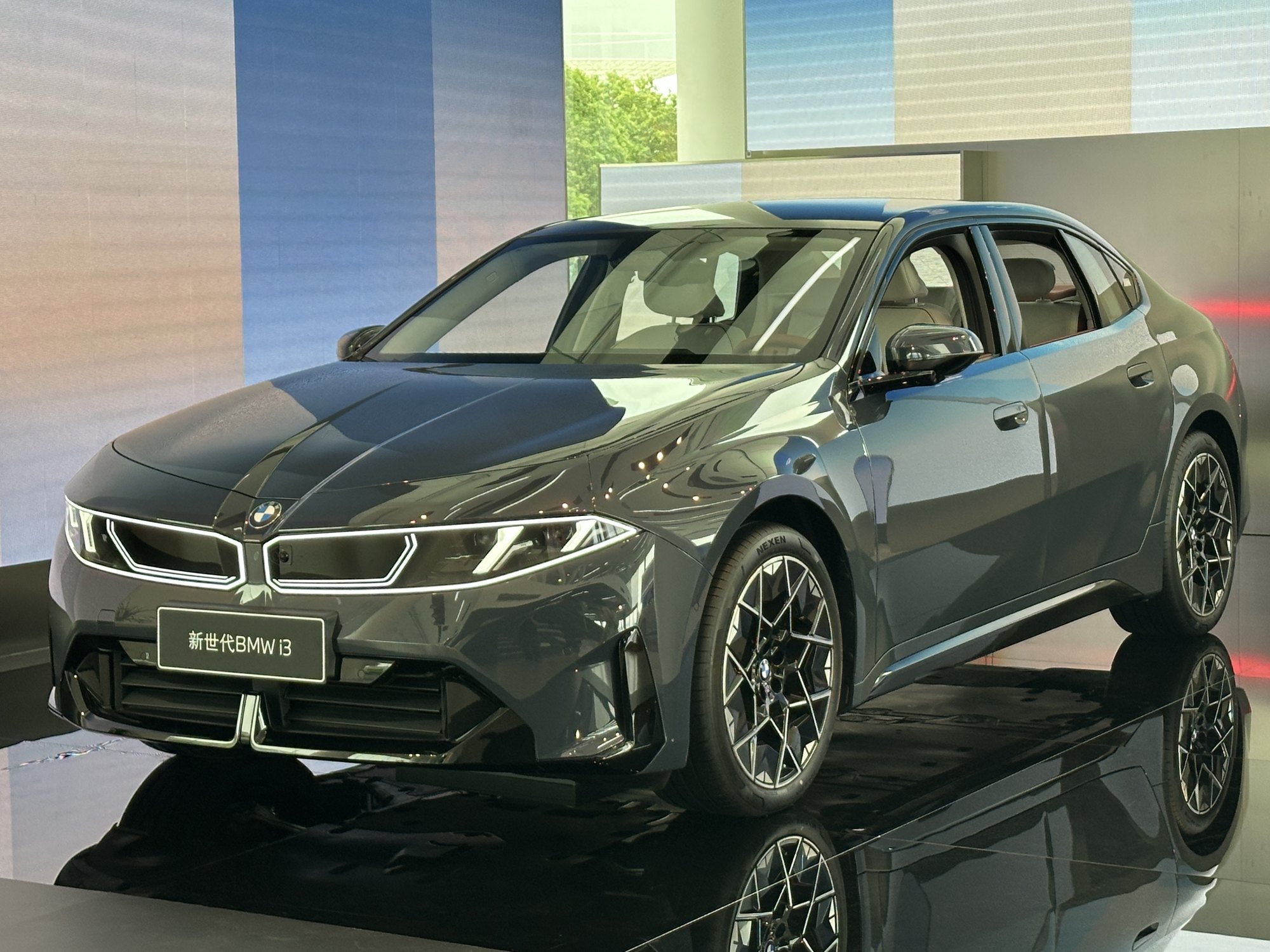 A dark grey new-generation BMW i3 electric sedan with illuminated kidney grille on a glossy display stand, with a sign reading 新世代BMW i3.